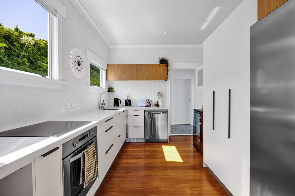 Modern white galley kitchen with timber accents, long stone benchtops, integrated appliances, and contemporary custom joinery by Newton Gordge Joinery.