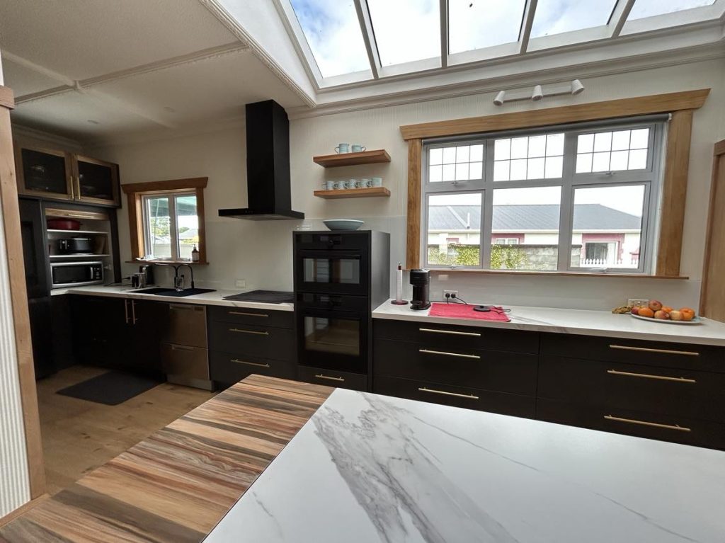 Black and timber kitchen with gold hardware, marble-look benchtops, skylight feature, and custom cabinetry by Newton Gordge Joinery.