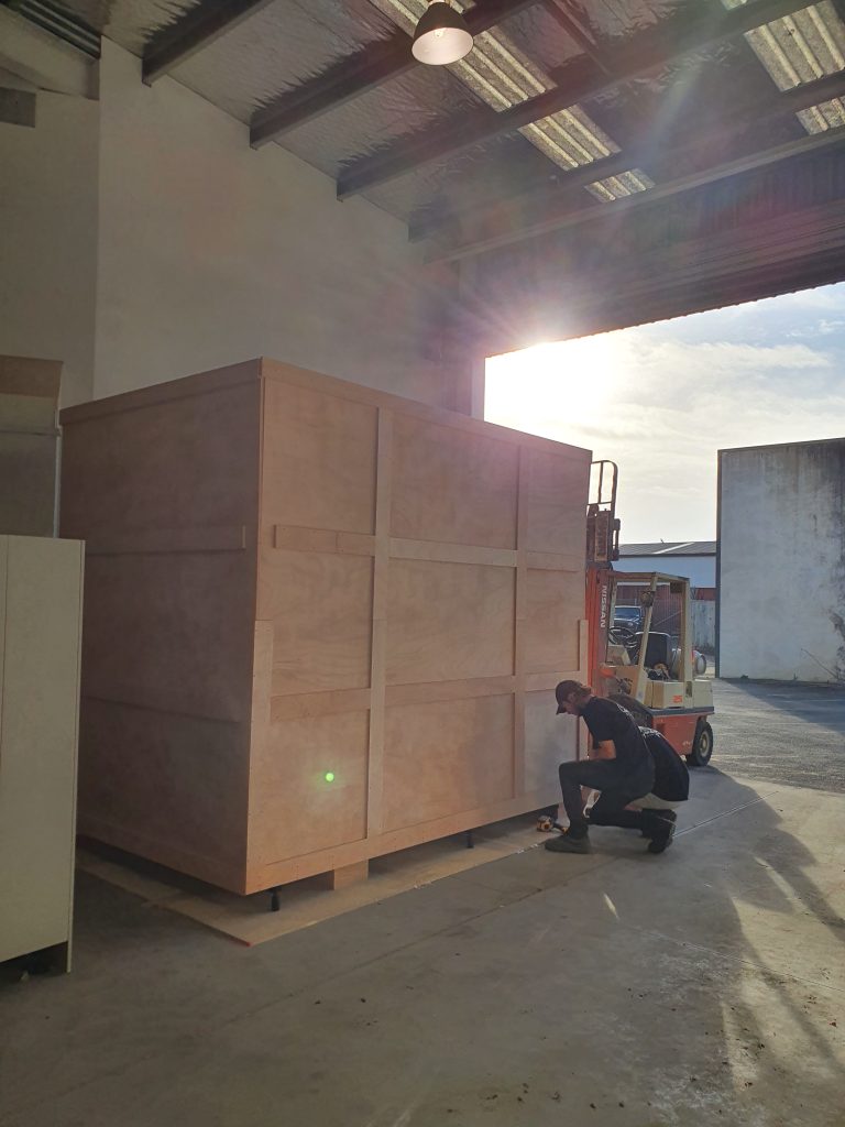 Newton Gordge Joinery crafts a large custom timber shipping crate inside their workshop, with a worker securing the base and a forklift positioned behind it.