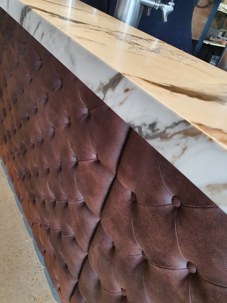 Close-up of a custom commercial bar front featuring deep-buttoned brown upholstery and a marble-look countertop crafted by Newton Gordge Joinery.