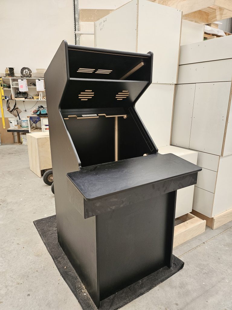 Black custom-built arcade cabinet frame under construction in a Newton Gordge workshop.
